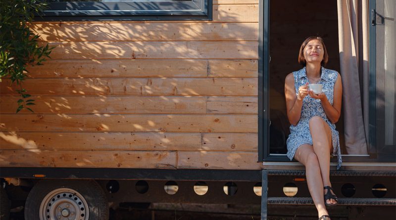 Image of a women sat in the doorway of a tiny home to support tiny house villages article