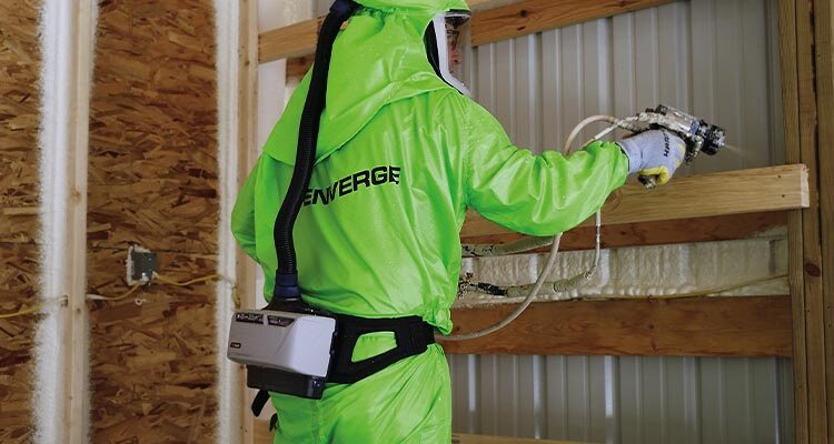 Worker in green Enverge protective overalls using spray foam on a wall