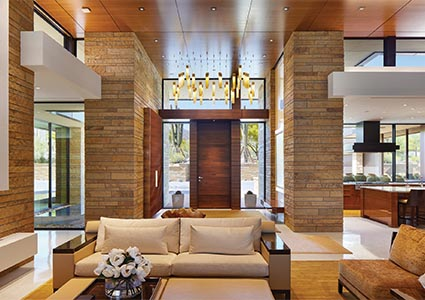 A collection of Shakúff pendants hang from quartered American walnut ceiling panels by Fritz Cabinetry in the entryway. Clean lined yet cozy, the Liaigre sofa and chair continue the warm, modern vibe.