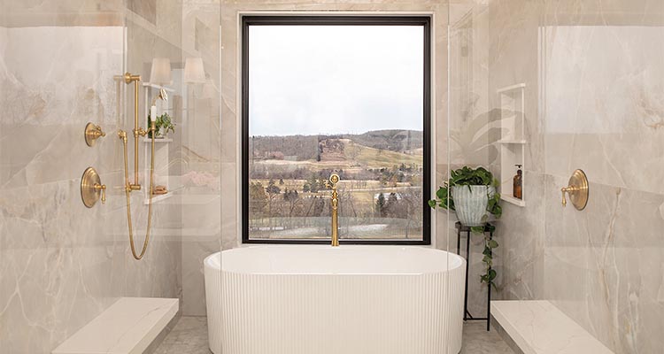 Luxurious bathroom with elegant marble walls, gold fixtures, freestanding bathtub, and large window overlooking scenic view, featuring wooden cabinetry and indoor plants.