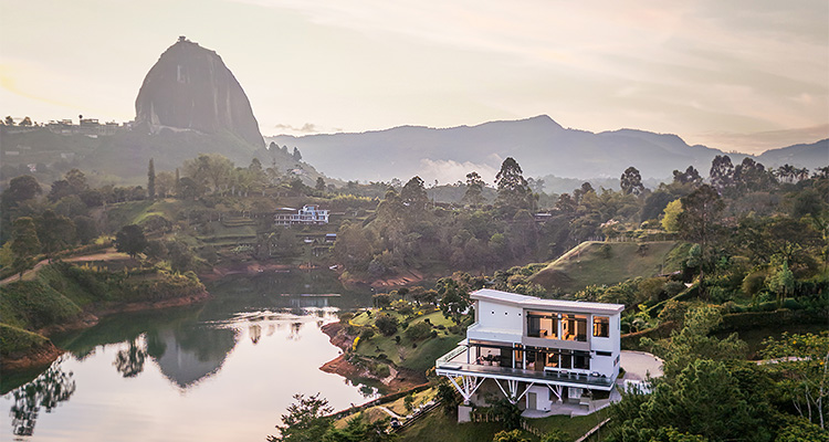 Representing the best of homebuilding excellence, Schenkar Custom Homes redefines luxury on a global scale a modern, luxurious house situated on the shore of a lake, likely in Guatapé, Colombia