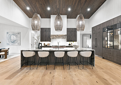 a modern kitchen with a prominent island, featuring white bar stools and dark cabinets