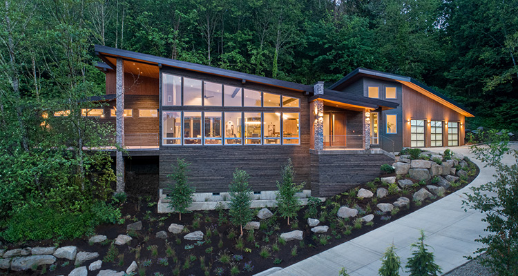 a striking modern, single-story home nestled into a lush, wooded hillside at dusk
