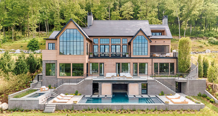 a large, modern residential house featuring extensive glass windows, a multi-level terrace, and a swimming pool