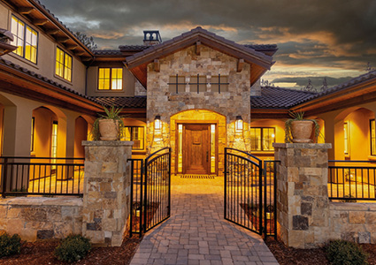 A luxurious Tuscan-style home features a prominent stone facade, a arched entryway, and wrought iron fencing
