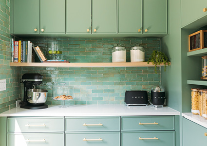 a kitchen featuring mint green cabinets, a glossy green Zellige tile backsplash, and light wood open shelving