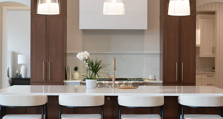 a modern kitchen centered around a large kitchen island with four low-backed white bar stools arranged along its front