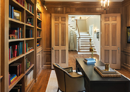 a classic, wood-paneled home office or library looking out toward an entryway.