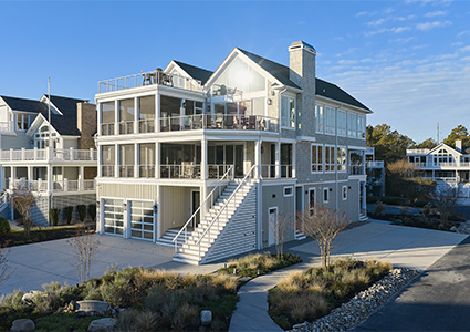 a large, modern multi-story coastal house on a sunny day under a blue sky with light clouds.