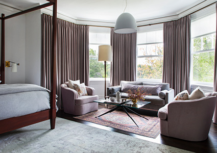 a spacious, elegantly designed bedroom that includes a distinct seating area arranged within a large bay window