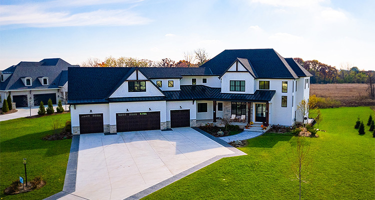 a large, two-story modern farmhouse style mansion under a clear blue sky