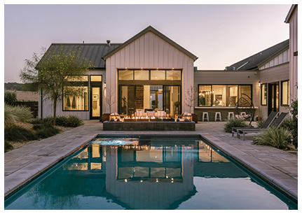 shows the backyard of a modern, luxury home at dusk, featuring a large swimming pool and an outdoor entertainment area