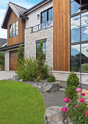 a modern custom-built home exterior that blends natural stone veneer, vertical wood siding, and large black-framed windows