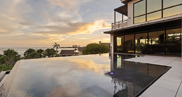 Bluewater Construction redefines luxury homes through innovation, exceptional team culture, and unwavering craftsmanship for discerning clients a modern luxury villa featuring a large, elevated infinity pool that reflects the colorful sunset sky