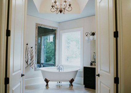 a traditional master bathroom featuring a white freestanding clawfoot bathtub centered in front of a window