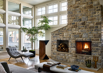 a modern living room featuring a towering, floor-to-ceiling natural stone fireplace wall with a built-in wood storage nook next to the firebox