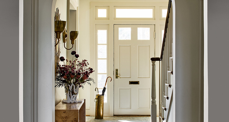 a traditional, warmly lit home entryway with a cream-colored paneled front door, sidelights, and a transom window