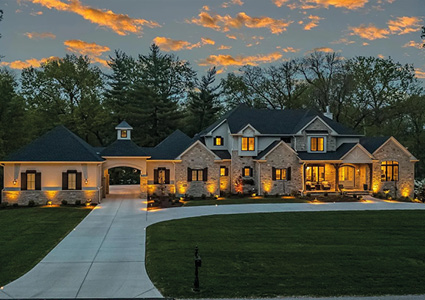 a large, custom-built luxury estate photographed during dusk or dawn under a dramatic orange and blue sky