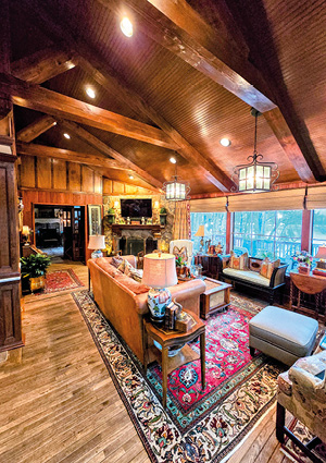 a cozy living room with a vaulted wood-beamed ceiling, a stone fireplace, and large windows looking out to trees