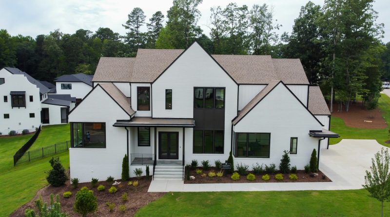Modern custom-built home with white exterior, landscaped garden and large black-framed windows.