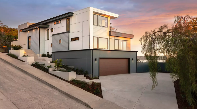 Modern custom home with a contemporary garage door and landscaped driveway at sunset.