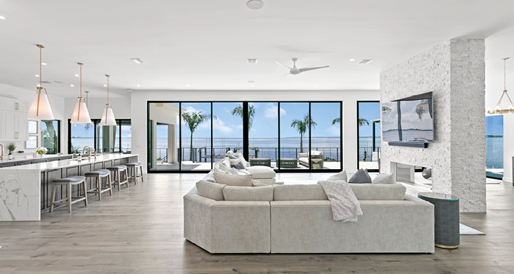 a luxurious, open-concept great room combining a living area and kitchen, heavily defined by its seamless indoor-outdoor integration and sweeping waterfront views