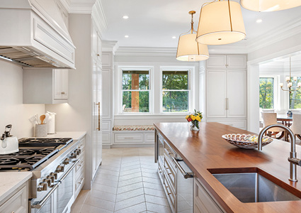 a bright, traditional-style kitchen featuring a long wooden-topped kitchen island, white cabinetry, a built-in window bench, and a large professional range stove