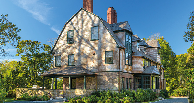 a large, multi-story house built in the architectural style of a Shingle-style home or a grand coastal cottage