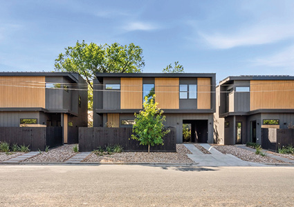 a row of three modern, two-story townhomes or detached houses situated side by side along a paved residential street