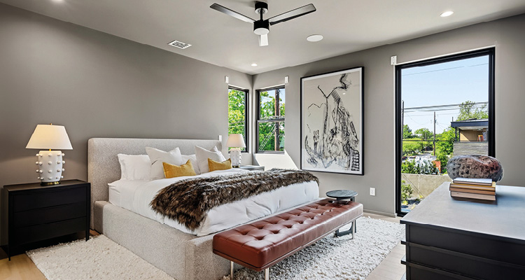 A contemporary bedroom with a grey color palette, featuring a bed with a faux-fur throw, a tufted brown leather bench, and black nightstands