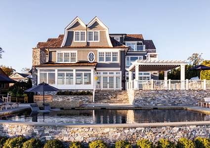 a large, multi-story luxury coastal home featuring a backyard swimming pool and extensive stone landscaping