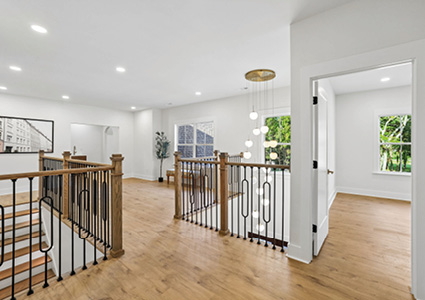 the upper-floor hallway and stair landing of a modern residential home featuring light wood-look flooring, a wooden and black metal balustrade, and a modern cascading bubble or globe chandelier