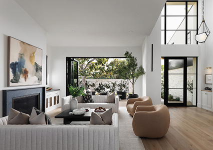 a modern, open-plan living room featuring a white tufted sectional sofa, curved beige armchairs, a dark wood coffee table, a black fireplace, and large black-framed glass sliding doors opening to an outdoor patio