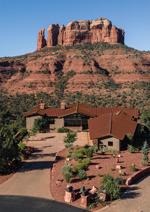 a striking southwestern landscape featuring a custom, multi-level home nestled directly below the iconic red rock formations of Sedona, Arizona