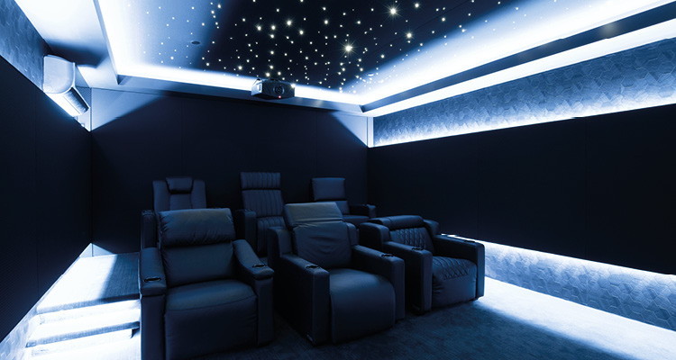 a dark, tiered home cinema room with black leather reclining armchairs, a fiber-optic starfield ceiling, and blue LED perimeter cove lighting