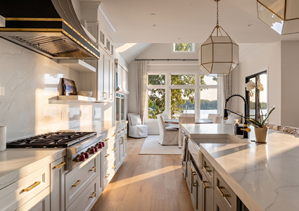 a modern luxury kitchen featuring a large white marble waterfall-edge center island, a professional-grade range with a custom hood, and an open-concept dining area overlooking a scenic view