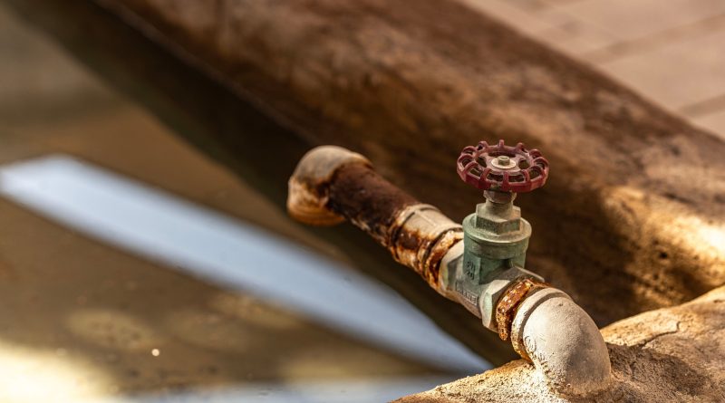 Close-up of a corroded water pipe and valve, illustrating aging infrastructure on a construction site.