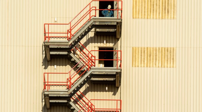 Construction workers using an external fire escape staircase at an industrial building.